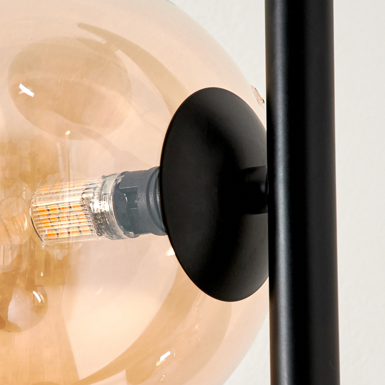 Nahaufnahme einer Lampe. Die Glühbirne befindet sich in einer Glaskugel. Schwarzer Metallpfosten rechts.