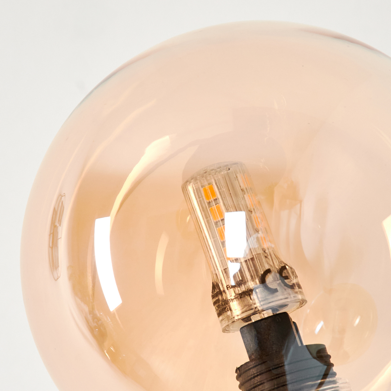 Nahaufnahme einer bernsteinfarbenen Glühbirne mit LED-Licht im Inneren, vor weißem Hintergrund.