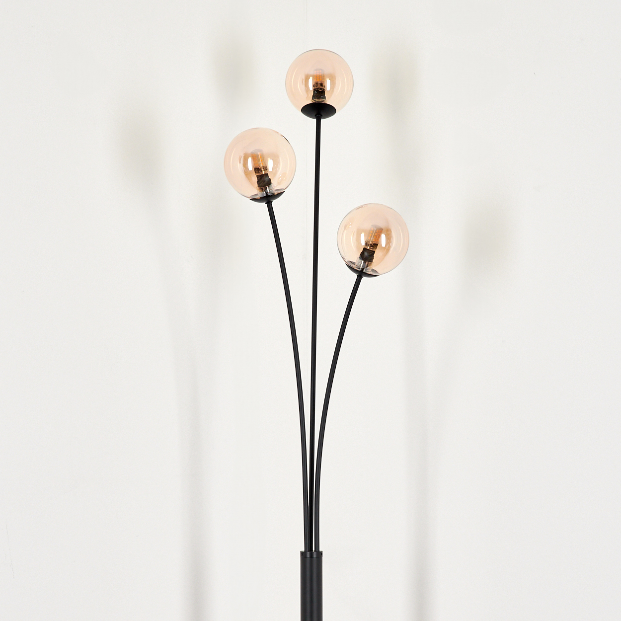 Eine Stehlampe mit drei bernsteinfarbenen Kugeln. Die Lampe befindet sich auf weißem Hintergrund.