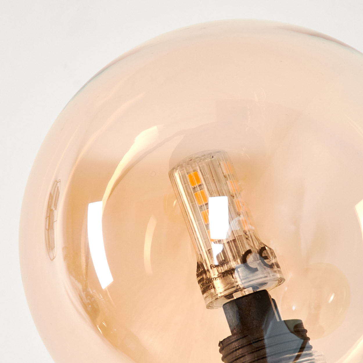 Nahaufnahme einer bernsteinfarbenen Glaskugelleuchte mit einer internen LED-Glühbirne, die den Sockel der Glühbirne zeigt.