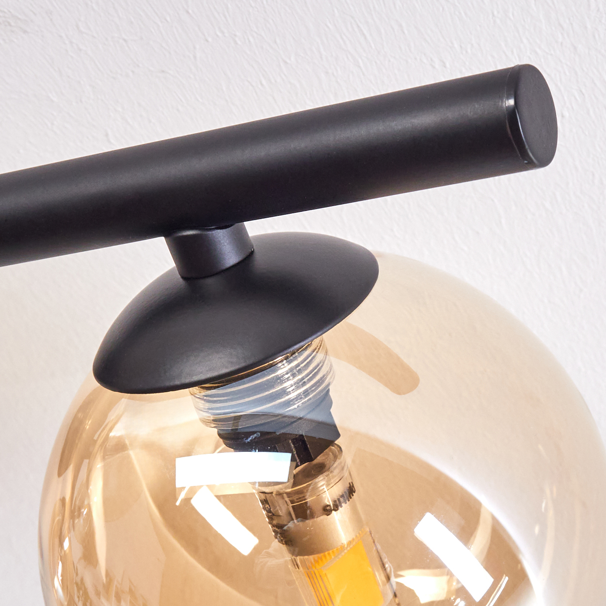 Nahaufnahme einer schwarzen Lampe mit Glasschirm, der eine warme Glühbirne zeigt.