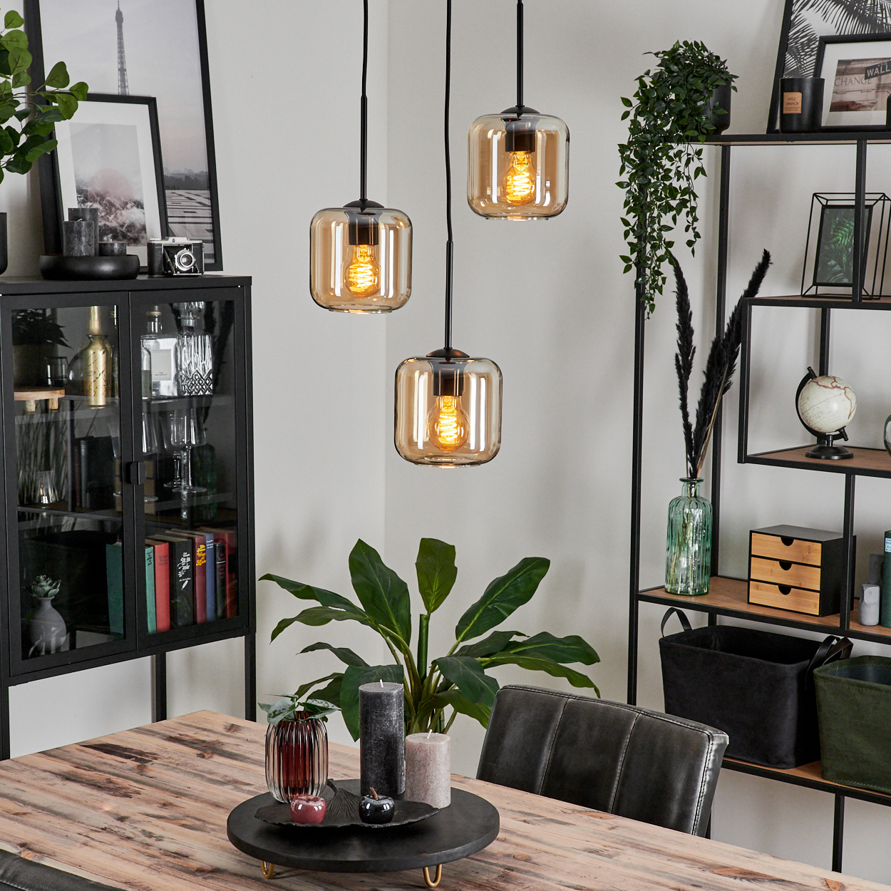 Drei Hängelampen mit bernsteinfarbenen Glasschirmen über einem Holztisch mit Dekoration.