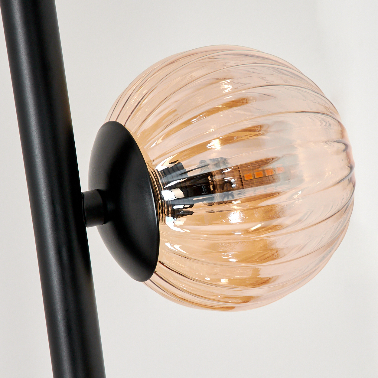 Nahaufnahme eines gerippten, bernsteinfarbenen Glaskugel mit schwarzer Halterung, Teil einer Lampe.