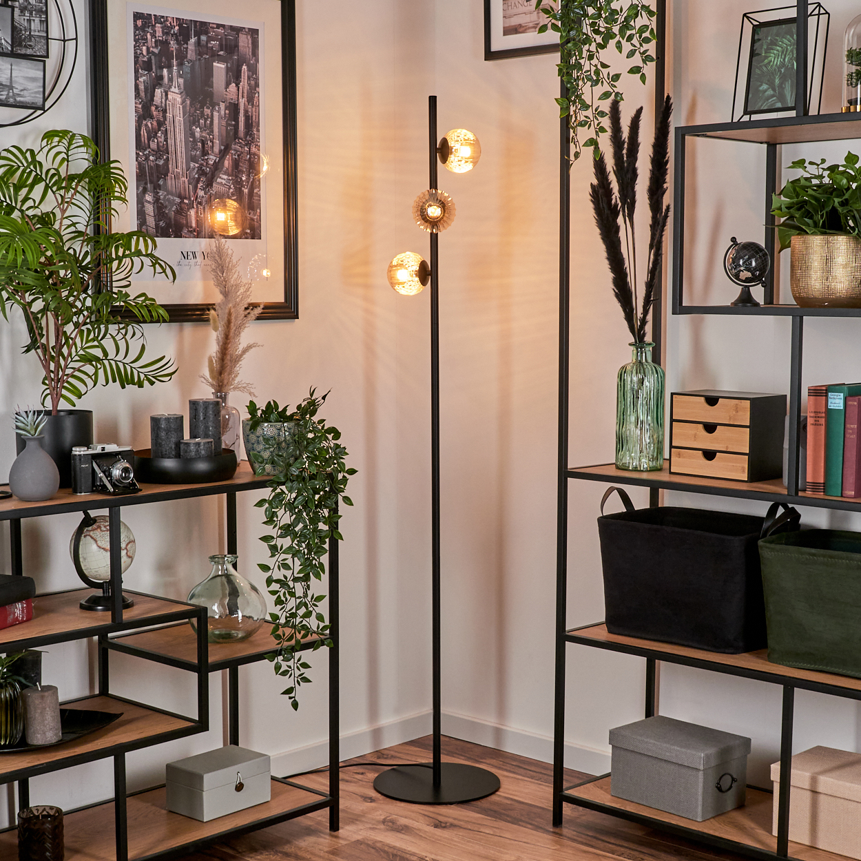 Stehlampe mit bernsteinfarbenen Kugeln in der Nähe von Regalen mit Dekor und Pflanzen, in einer Zimmerecke.
