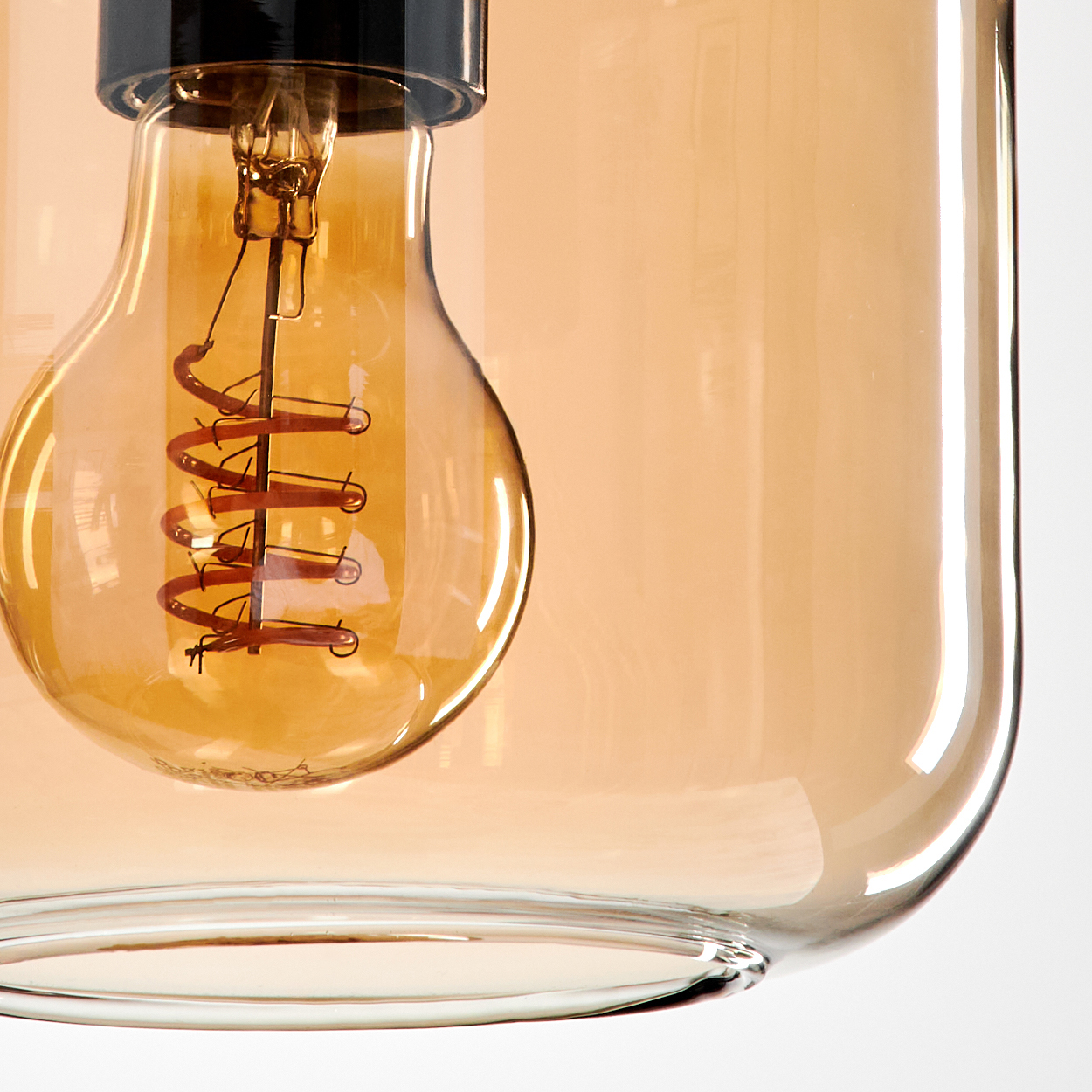 Nahaufnahme einer beleuchteten Edison-Glühbirne in einer bernsteinfarbenen Glas-Pendelleuchte, die den Wendel zeigt.
