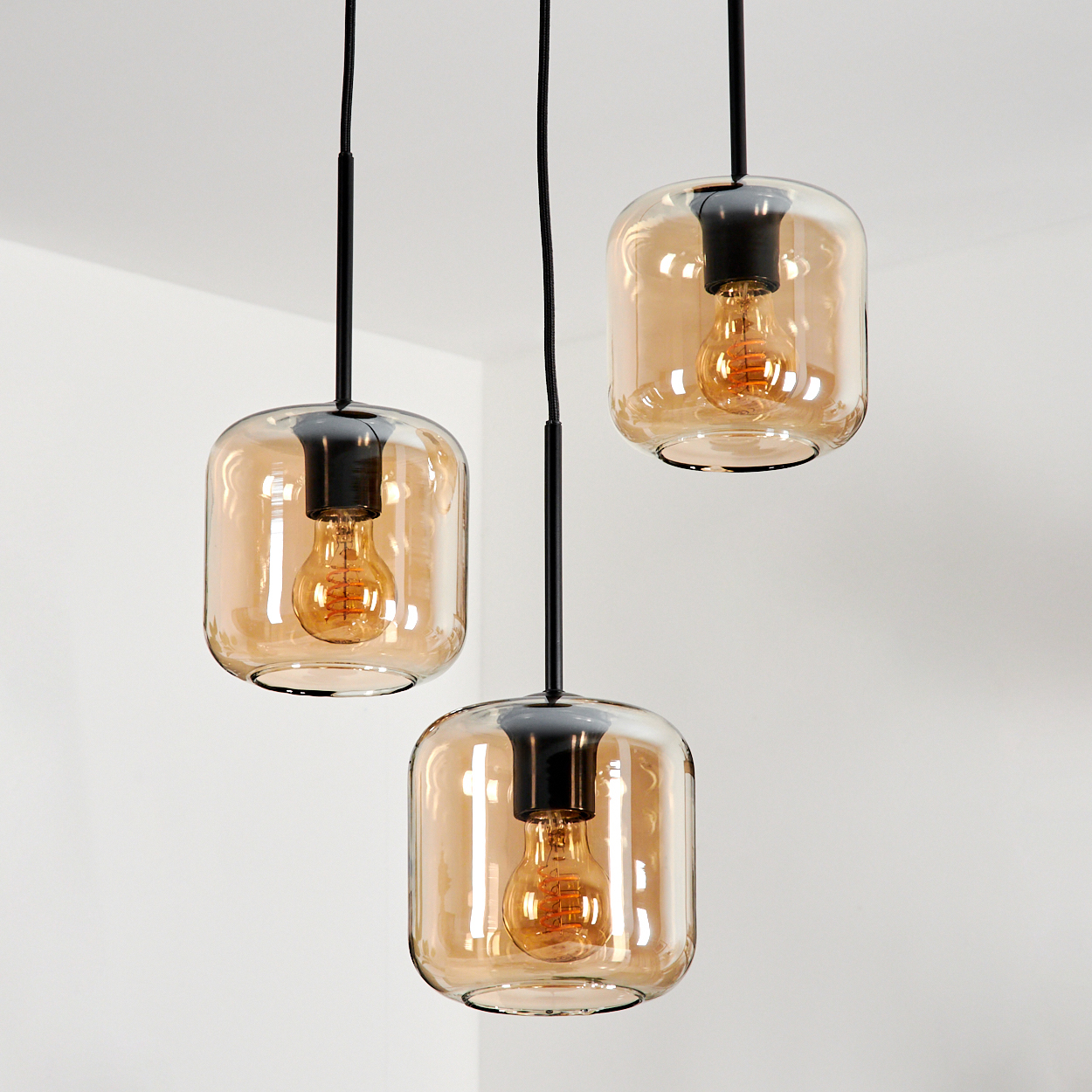 Drei Pendelleuchten mit bernsteinfarbenen Glasschirmen, beleuchtet, hängen von einer weißen Decke.