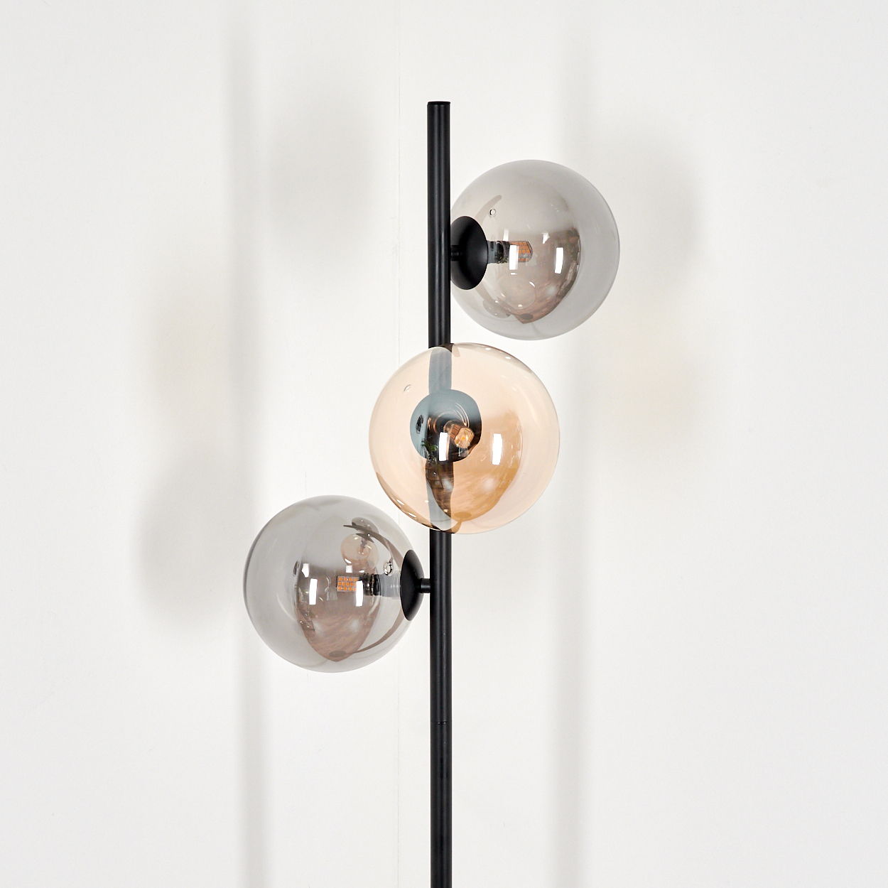 Eine schwarze Lampe mit drei Glasschirmen, die jeweils eine warme Glühbirne enthalten.