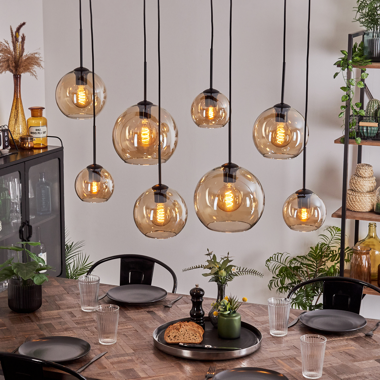 Esszimmer mit acht bernsteinfarbenen Glas-Pendelleuchten über einem Holztisch mit Dekorationen.