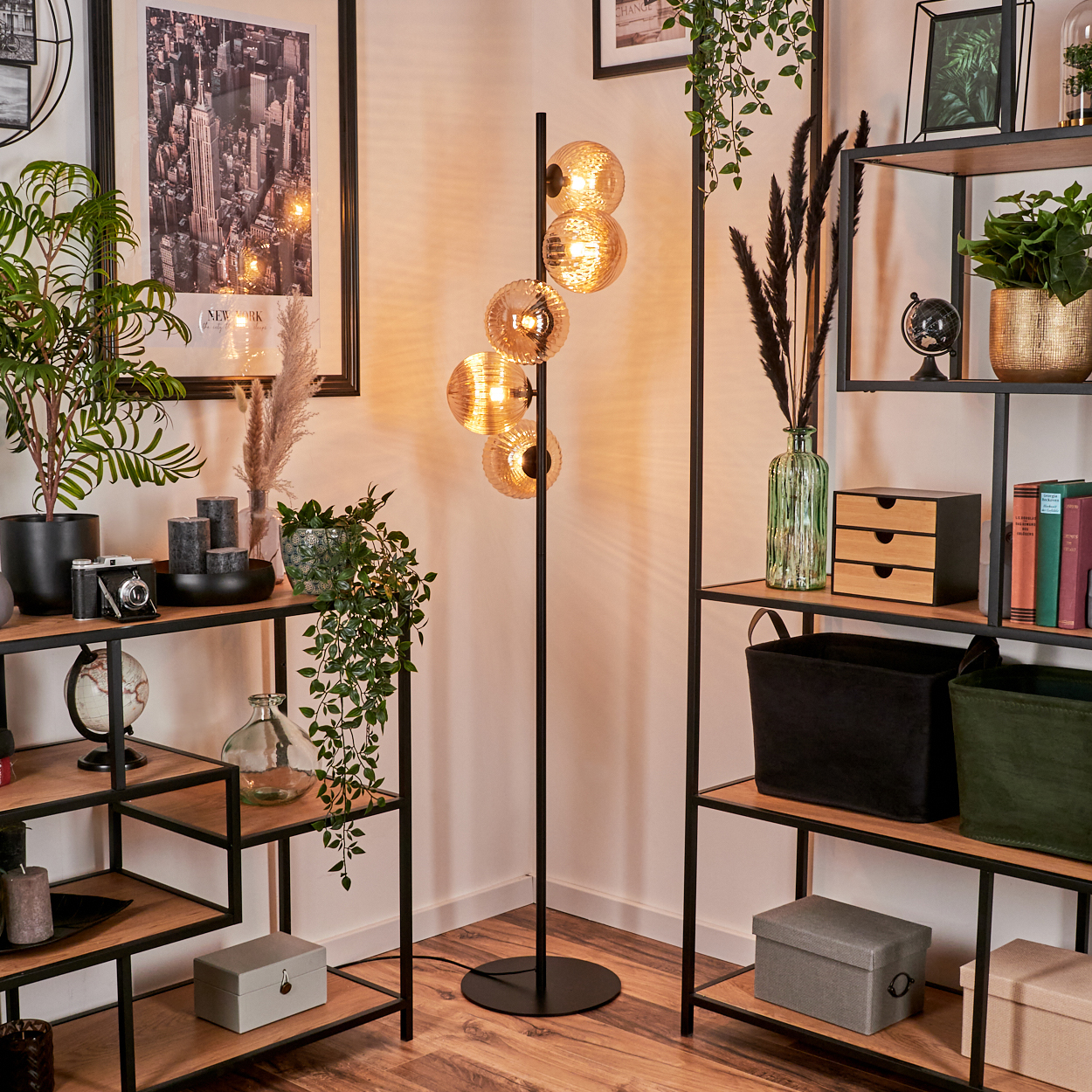 Eine Stehlampe mit mehreren bernsteinfarbenen Glaskugeln steht neben Regalen mit Deko.
