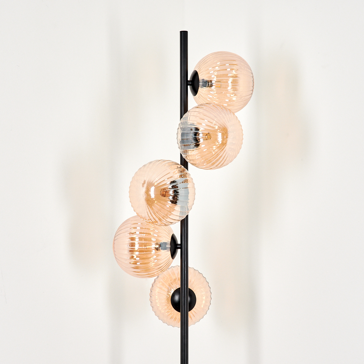 Eine hohe Stehlampe mit fünf bernsteinfarbenen Glaskugeln. Die Lampe hat ein schwarzes Metallgestell.