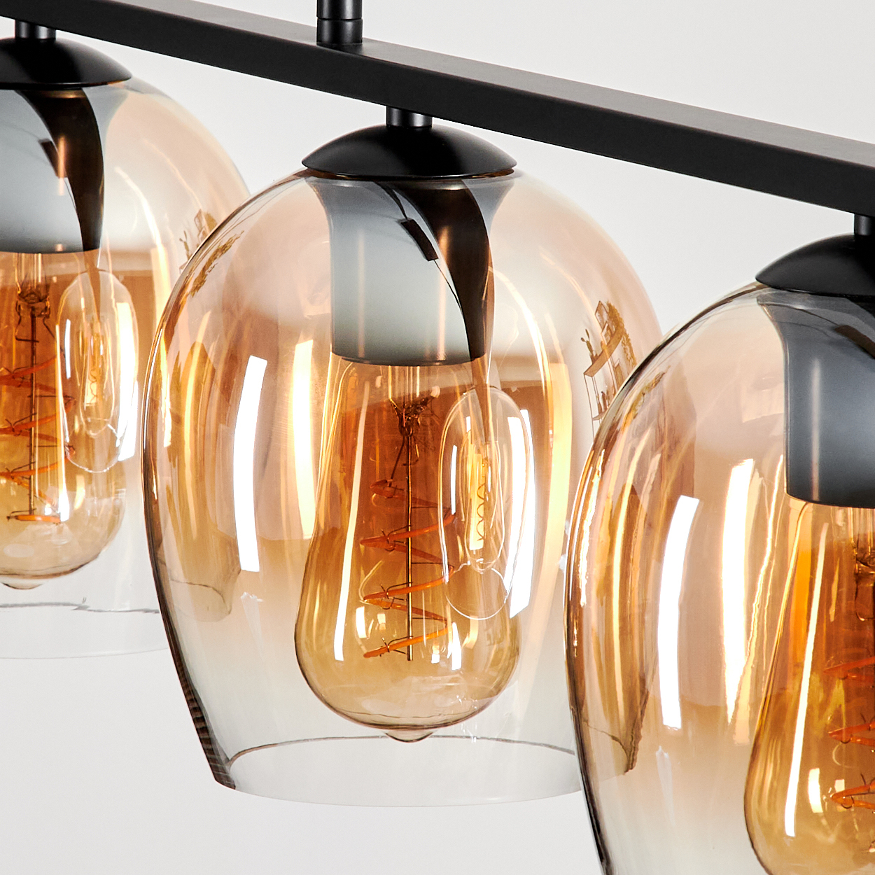 Nahaufnahme von drei Pendelleuchten aus bernsteinfarbenem Glas, die Glühbirnen im Inneren zeigend.
