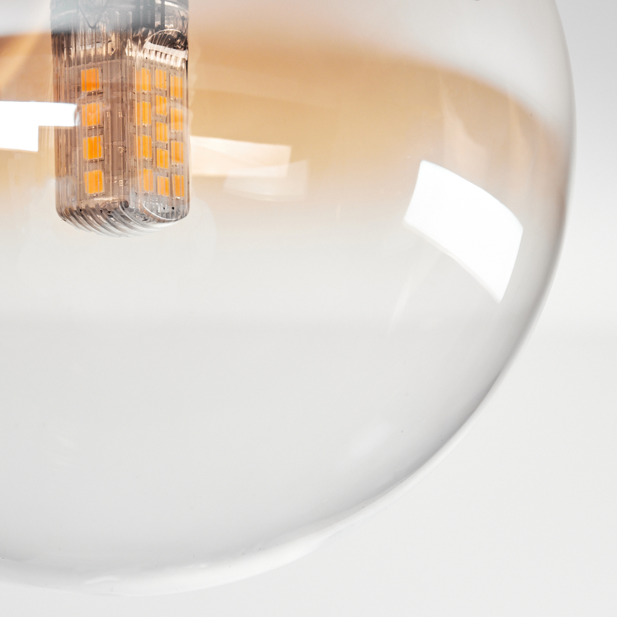 Nahaufnahme einer bernsteinfarbenen Glühbirne mit LED-Filament im Inneren, innerhalb eines Glaskolbens. Weißer Hintergrund.