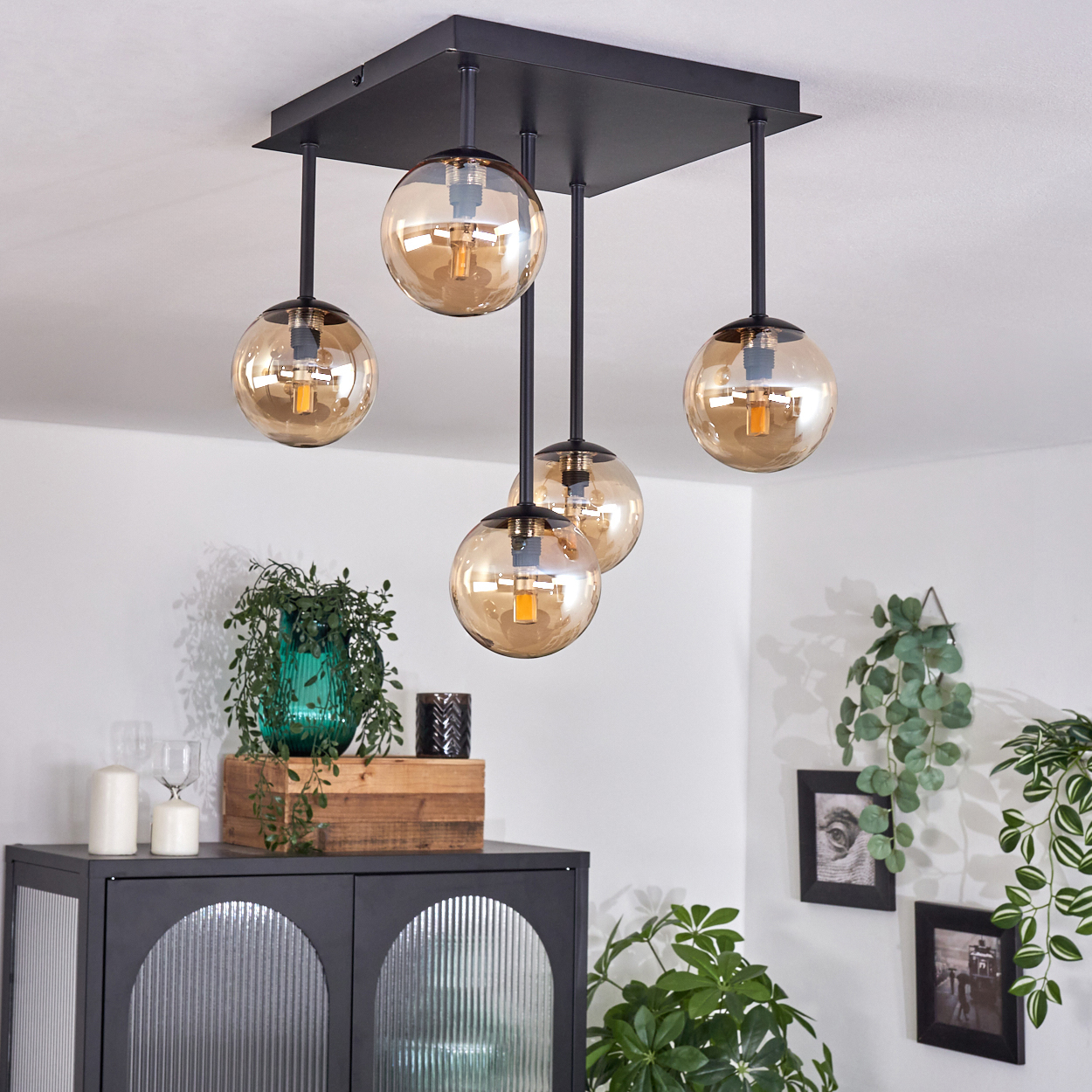 Schwarze Deckenlampe mit bernsteinfarbenen Glaskugeln. Pflanzen und Deko im Hintergrund.
