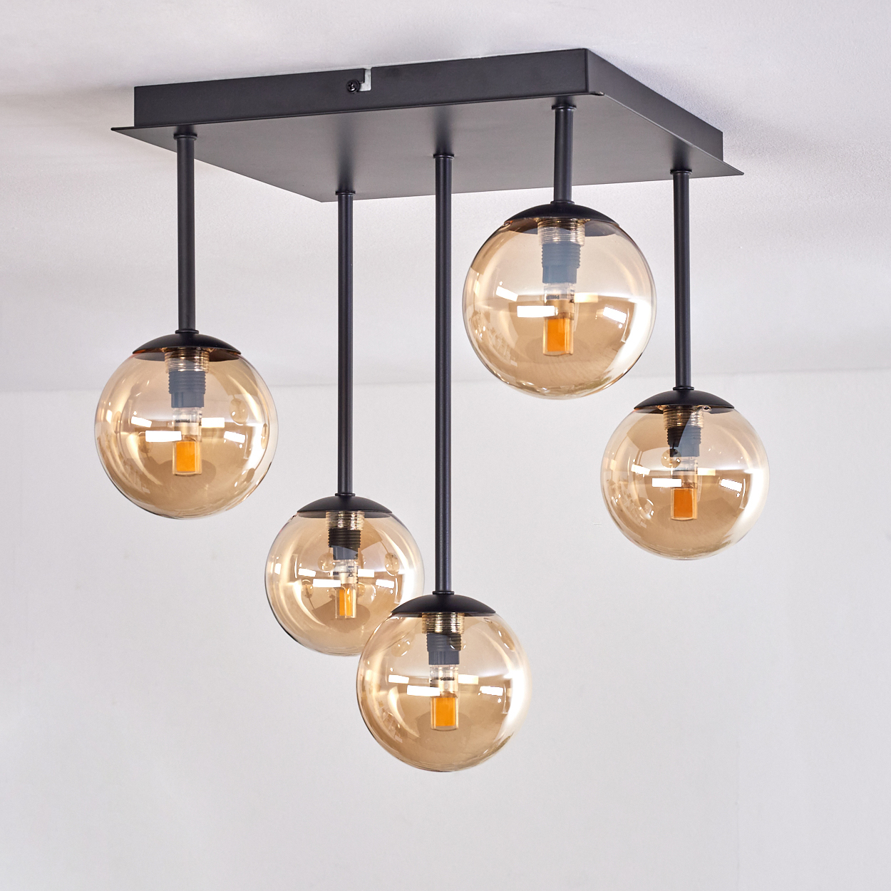 Schwarze Deckenlampe mit bernsteinfarbenen Glaskugeln auf weißem Hintergrund.