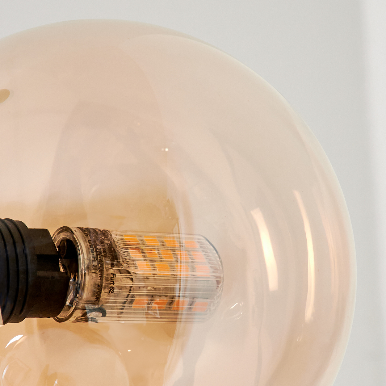 Nahaufnahme einer Glühbirne in einer bernsteinfarbenen Glaskugel. Die Glühbirne hat orangefarbene LEDs.