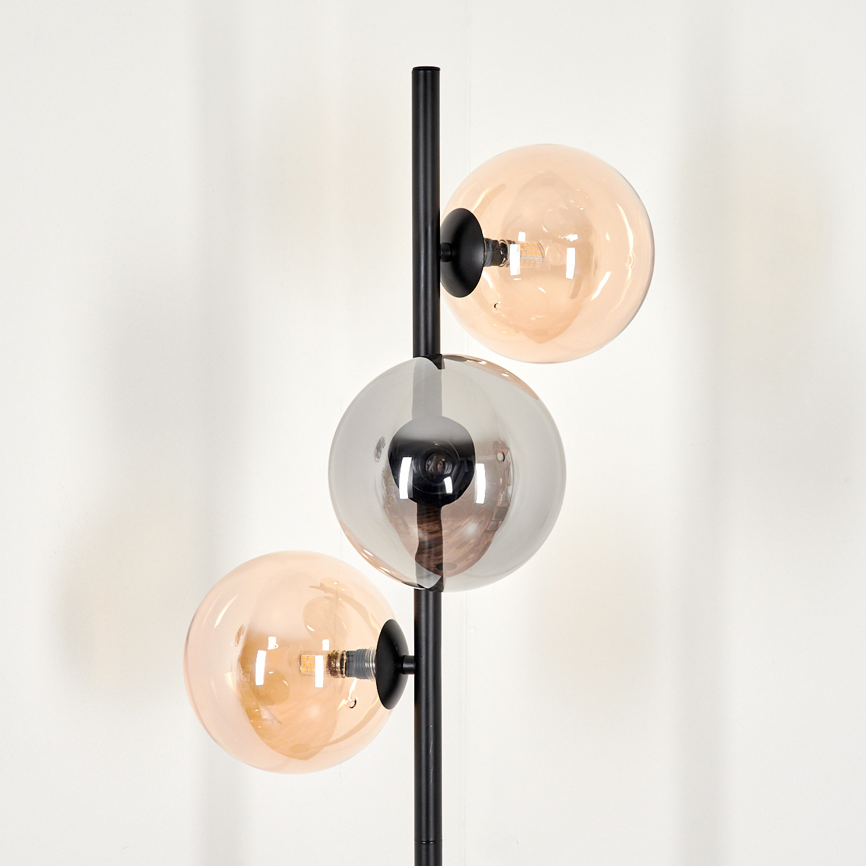 Stehlampe mit drei Glaskugeln, bernsteinfarben und silberfarben. Schwarze Stange. Weißer Hintergrund.