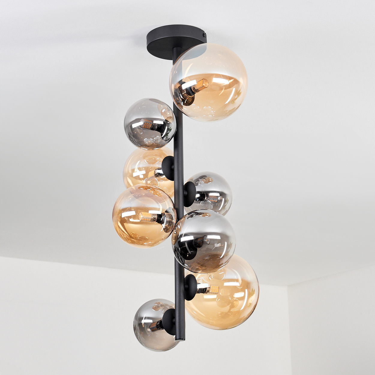 Schwarze Pendelleuchte mit Glaskugeln. Die Kugeln sind bernsteinfarben und silberfarben. Weiße Decke.