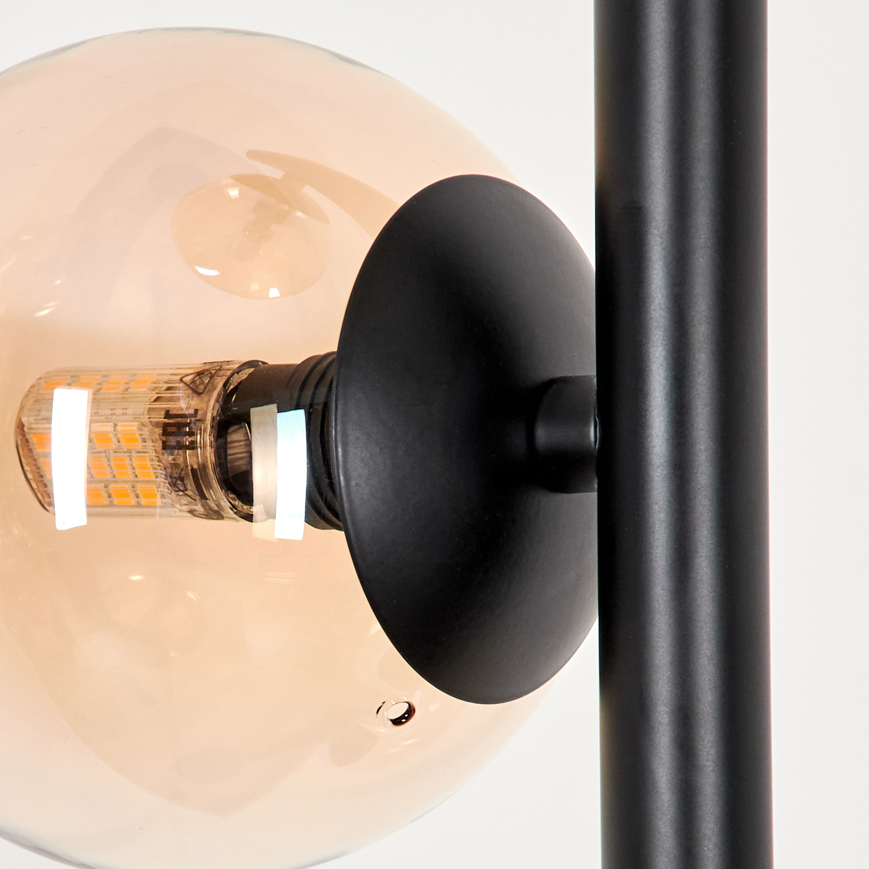 Nahaufnahme einer beleuchteten bernsteinfarbenen Glaskugel auf einer schwarzen Lampe. Die Glühbirne ist innen sichtbar.