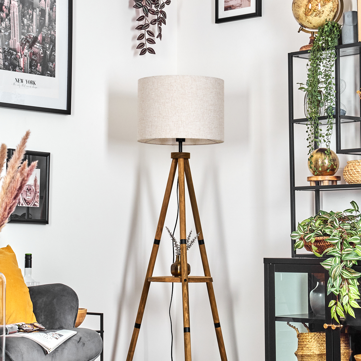 Holz-Stativlampe mit beigem Schirm, neben einem Stuhl. Der Raum hat ein Bücherregal und andere Dekorationen.