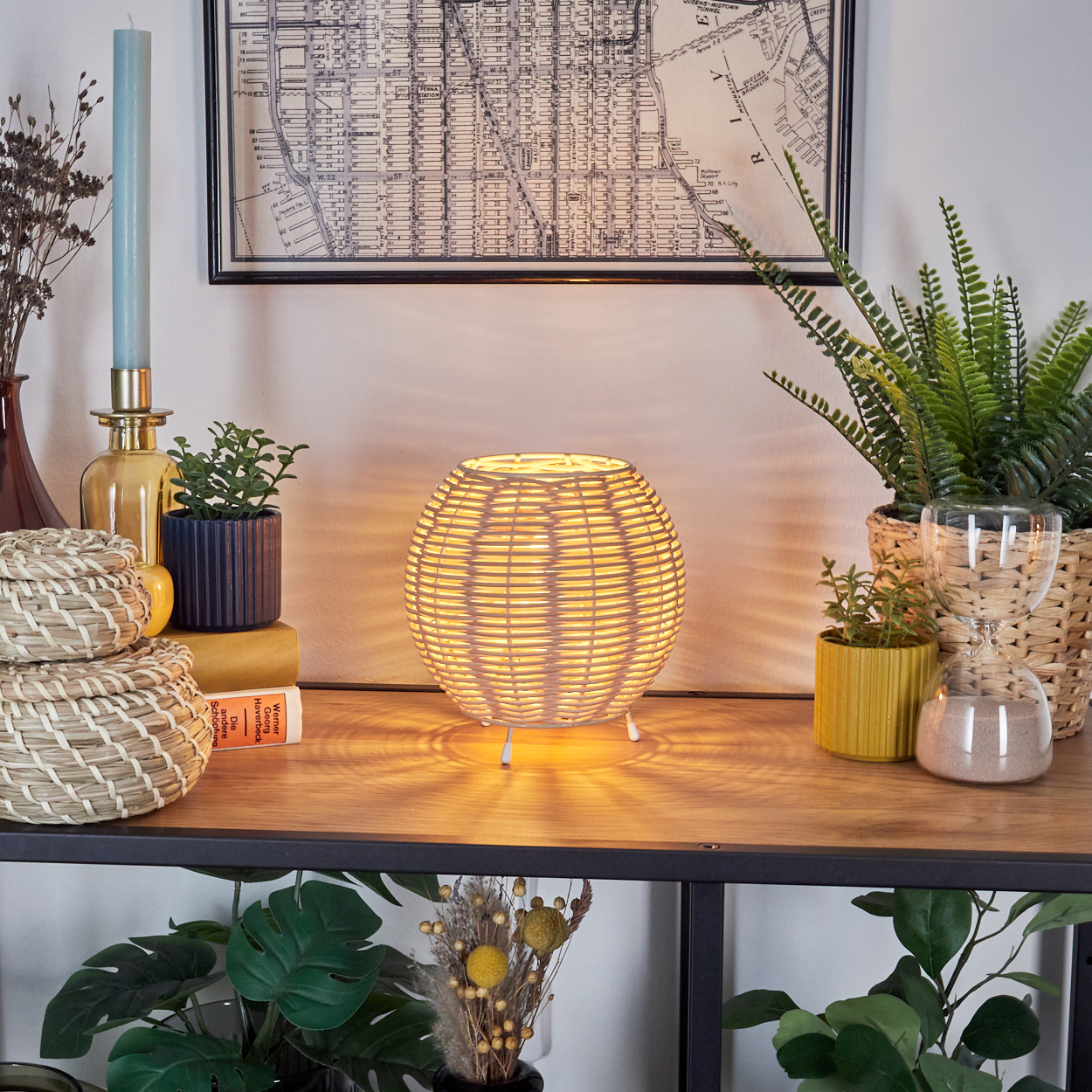 Gewebte Rattan-Tischlampe, Pflanzen, Bücher und dekorative Gegenstände auf Holzoberfläche.