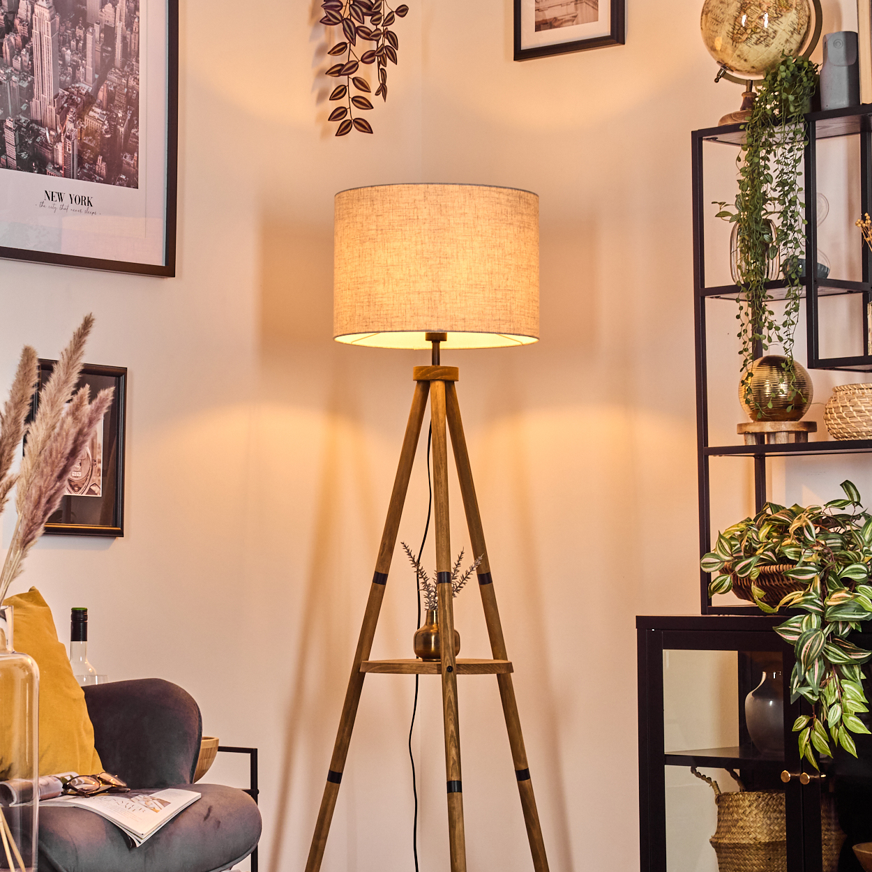 Eine beleuchtete Stehlampe steht in einem Raum. Die Lampe hat einen beigefarbenen Schirm und steht in der Nähe eines grauen Stuhls.