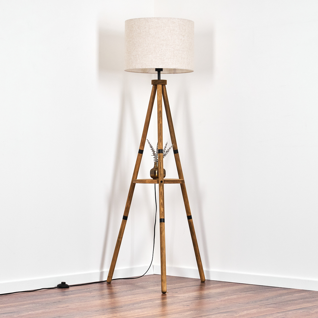 Holz-Stativ-Stehleuchte mit beigem Schirm, kleiner Vase mit Pflanzen, weißer Hintergrund.