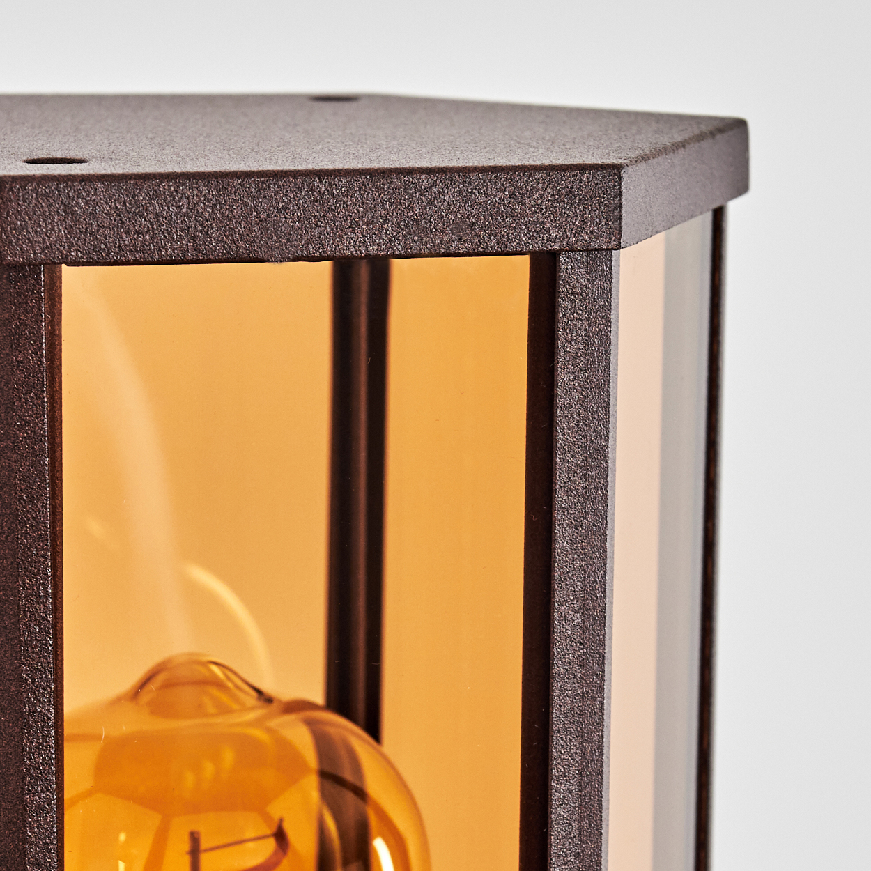 Nahaufnahme einer braunen Wandlampe mit bernsteinfarbenem Glas und sichtbarer Glühbirne.