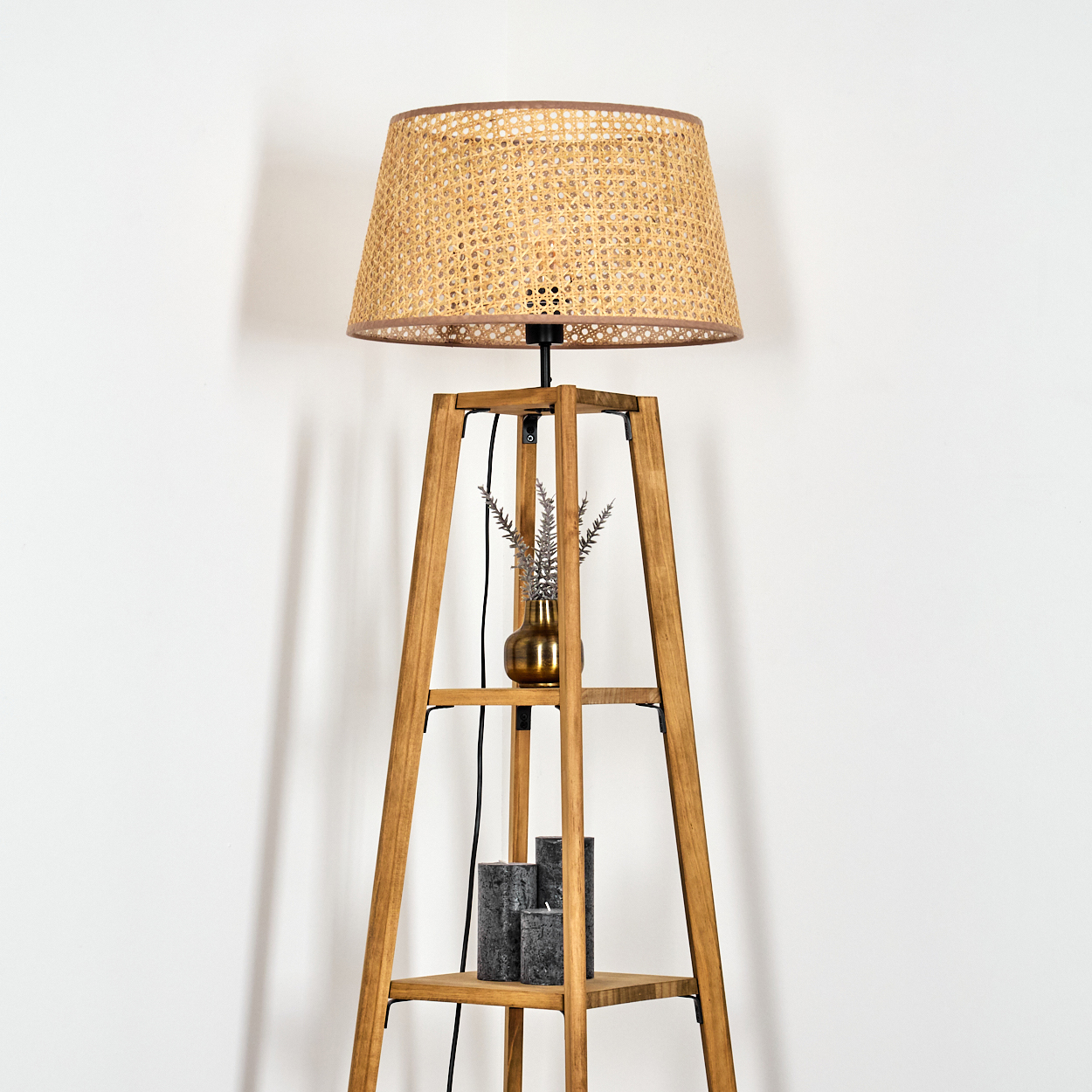 Holzlampe mit einem Korbschatten. Eine goldene Vase und Kerzen auf dem Regal darunter.