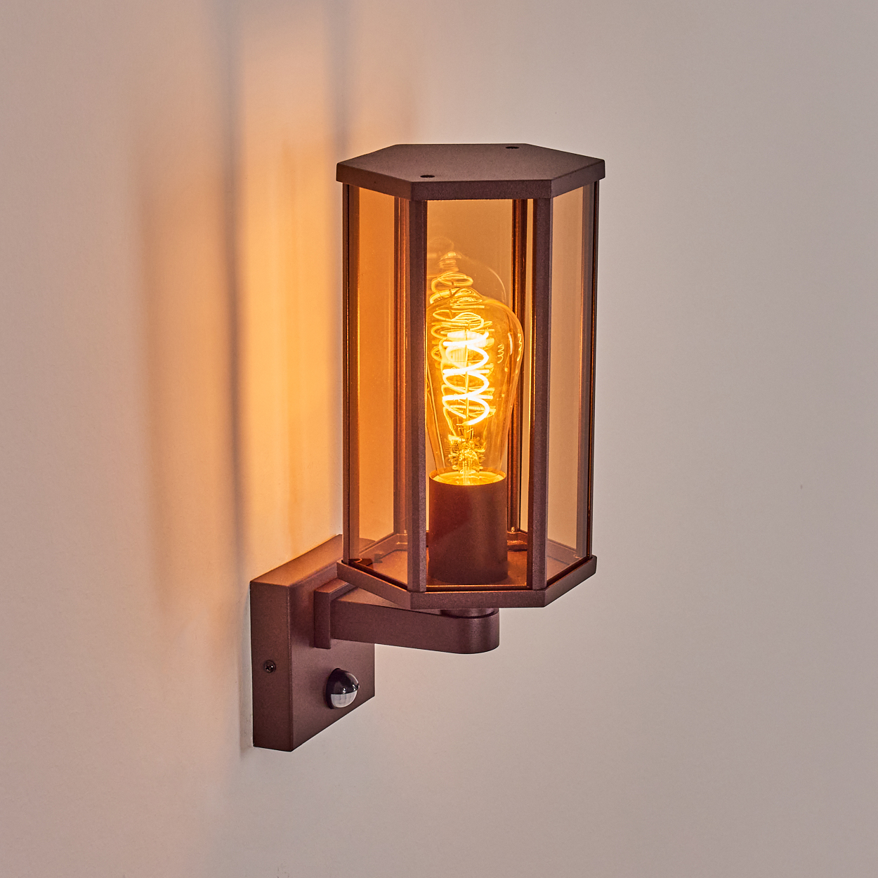 Nahaufnahme einer braunen Wandleuchte mit Glasschirm und Edison-Glühbirne. Bewegungssensor an der Wand.
