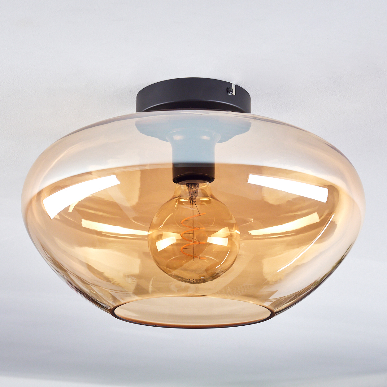 Nahaufnahme einer Deckenlampe mit goldenem Glasschirm und Glühbirne.