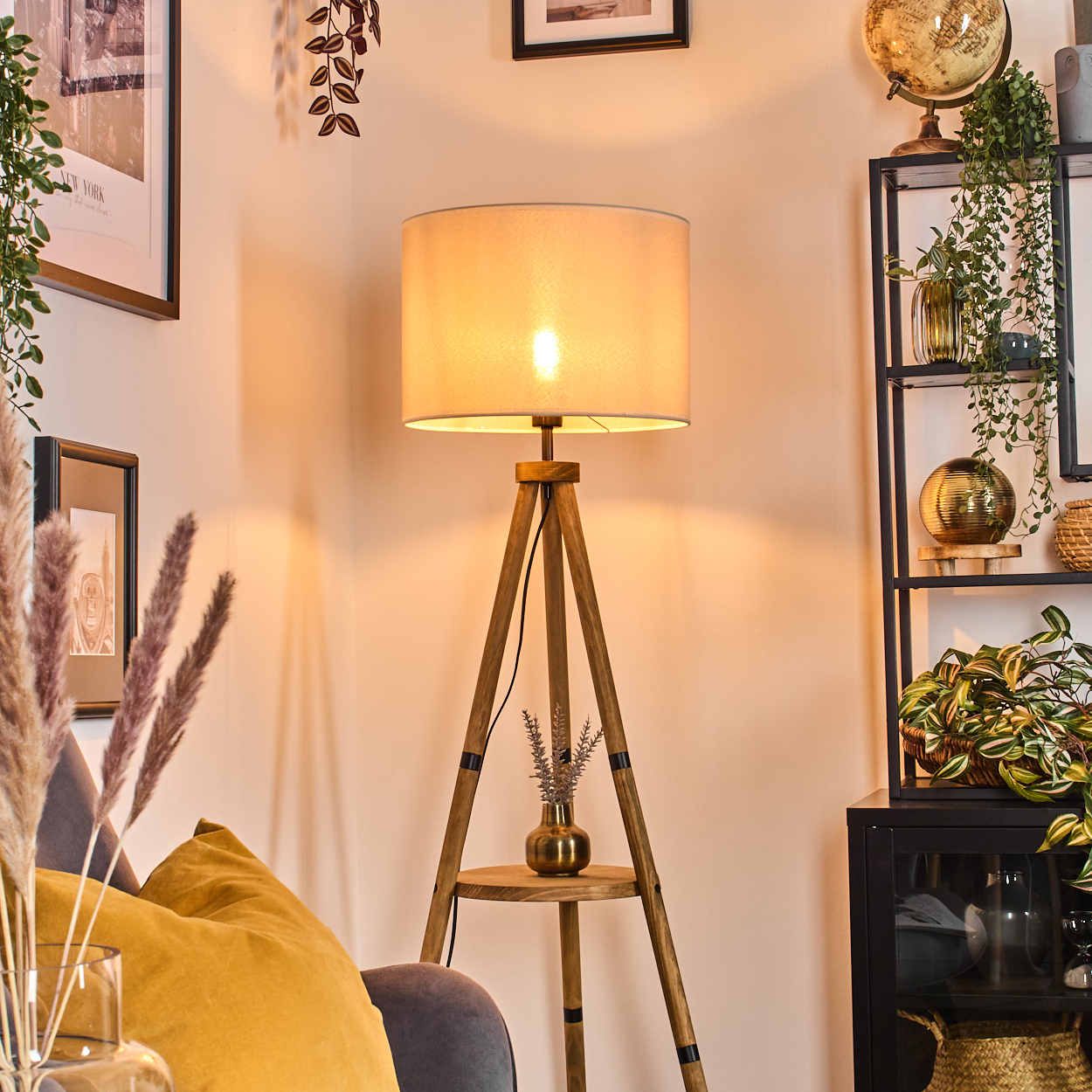 Eine Holzstativlampe mit Lampenschirm in einem gemütlichen Raum, umgeben von Dekoration und Pflanzen.