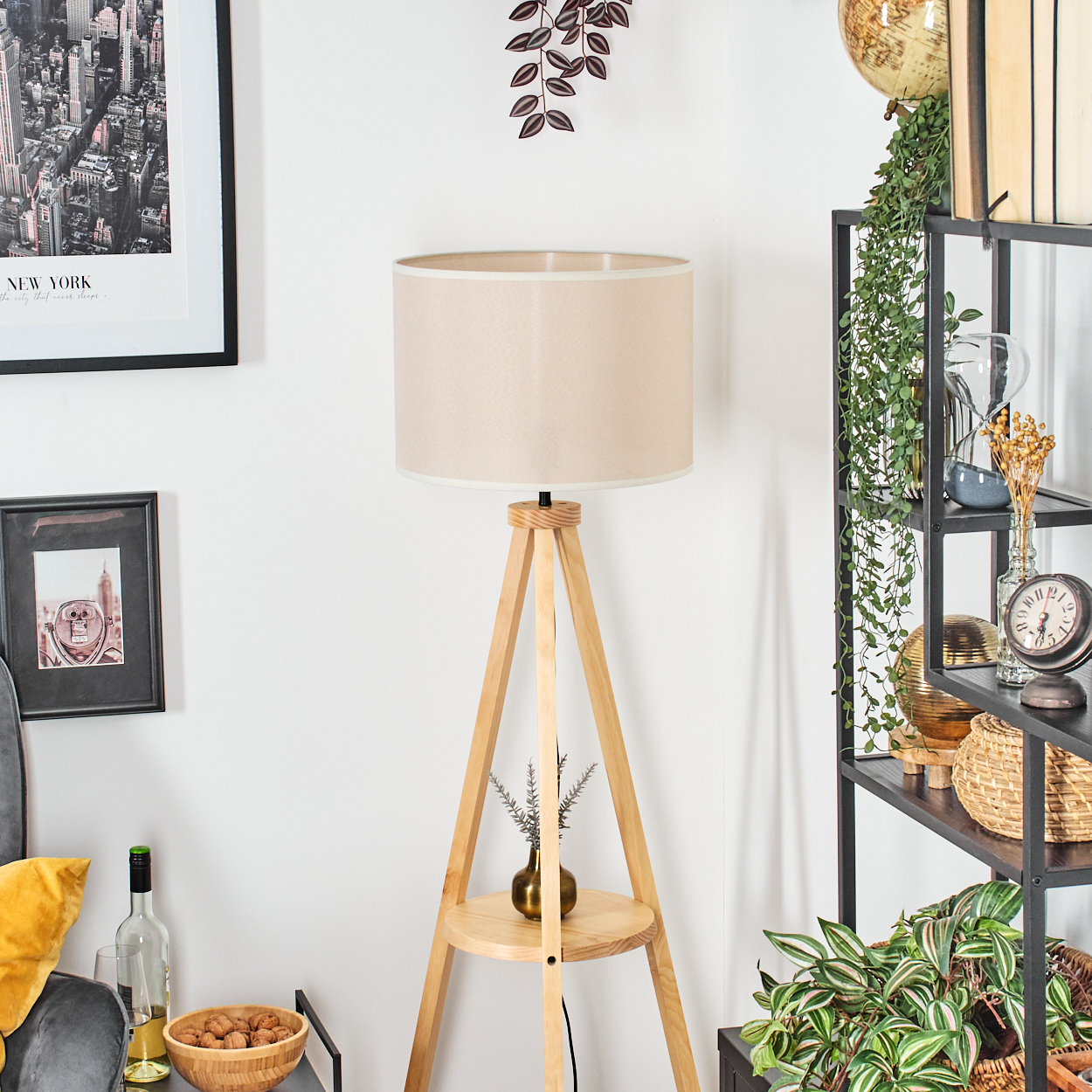 Dreibeinlampe in einem Raum. Beiger Schirm, Regal mit Deko, New York Poster. Helles Licht.