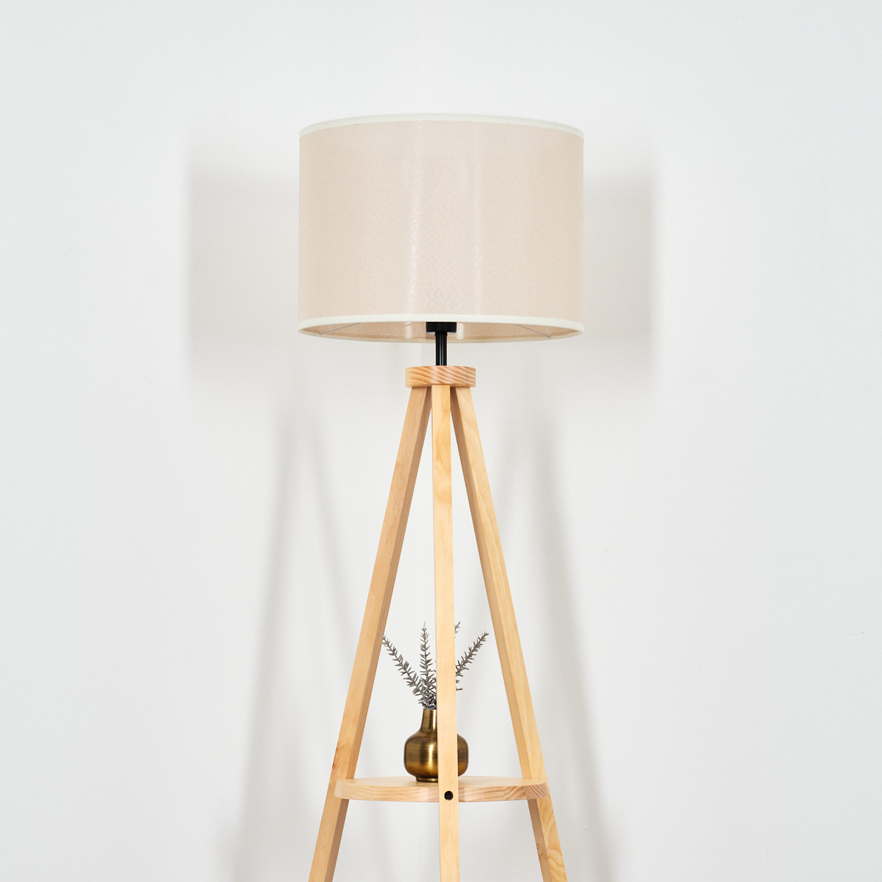 Stehlampe aus Holz mit beigem Lampenschirm vor weißer Wand.
