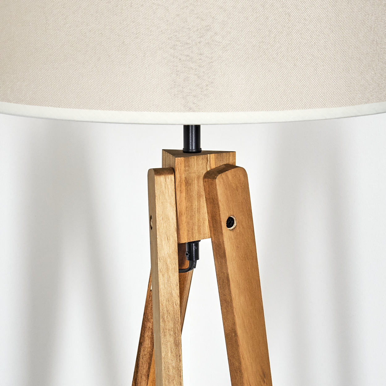Nahaufnahme einer Holz-Stativlampe. Beiger Lampenschirm. Weißer Hintergrund.