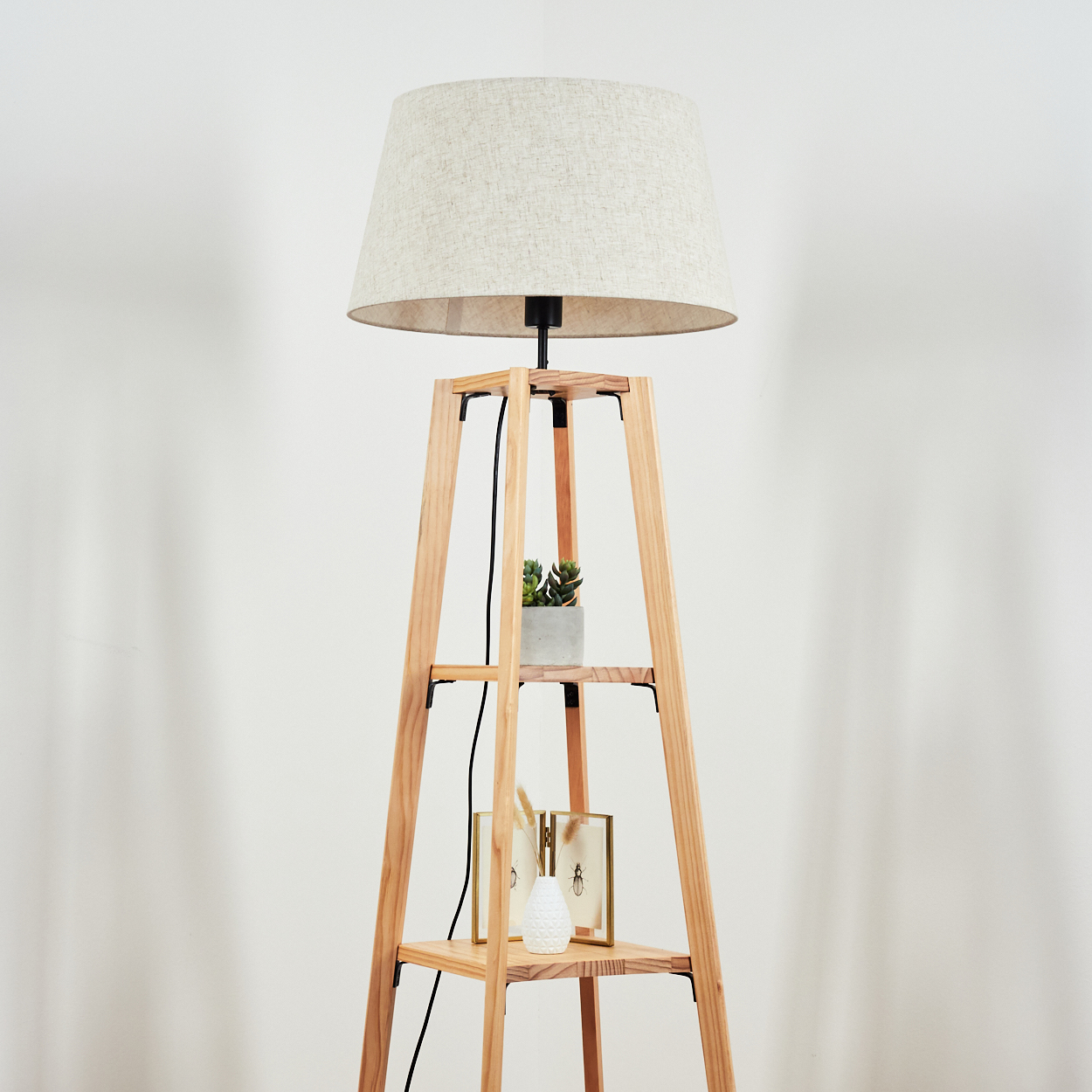 Stehlampe mit Lampenschirm und Regalen vor einer schlichten weißen Wand.