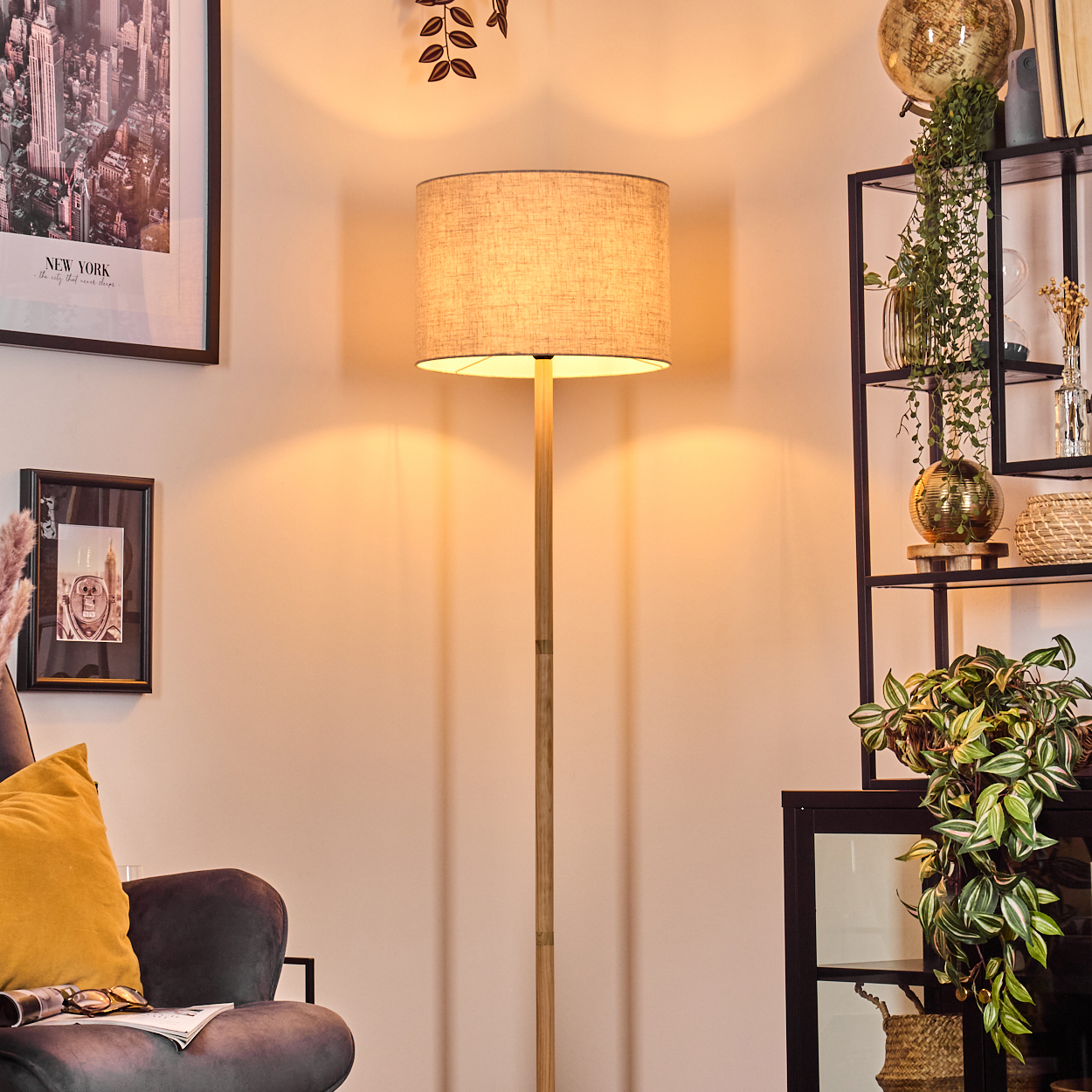 Eine Stehlampe mit Leinenschirm leuchtet, neben einem dunklen Stuhl und einem Regal mit Pflanzen.