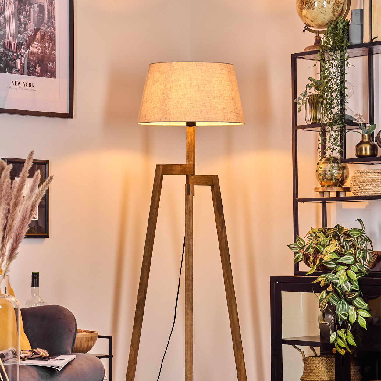 Tripod-Lampe in einem Raum. Lampe leuchtet, mit beigem Schirm. Innenraum mit Kunst und Pflanzen.