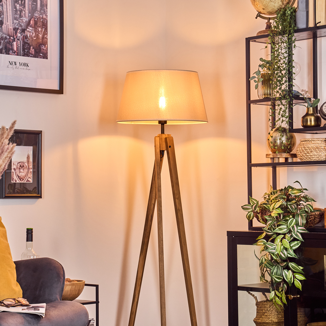 Stehlampe mit beigefarbenem Lampenschirm und Holz-Dreibeinbeinen in einem Wohnzimmer.