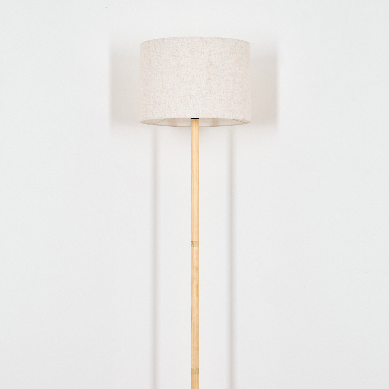 Stehlampe mit beigefarbenem Lampenschirm an einer Holzstange vor weißem Hintergrund.