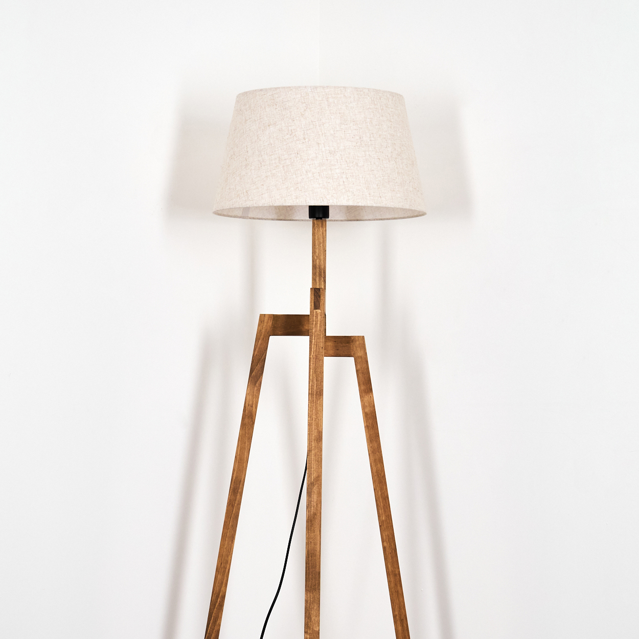 Holz-Stativlampe mit beigem Schirm. Schwarzes Netzkabel. Weißer Hintergrund.