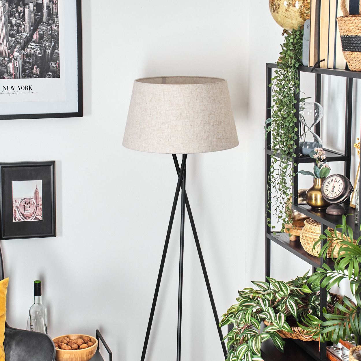 Ein Wohnzimmer mit einer Stehlampe. Ein schwarzer Rahmen mit einem New York City-Bild und ein Bücherregal sind vorhanden.