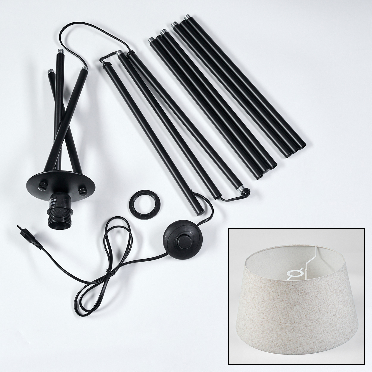 Zerlegte Lampenkomponenten. Schwarze Beine und Sockel, Netzkabel, Schalter und beiger Lampenschirm.