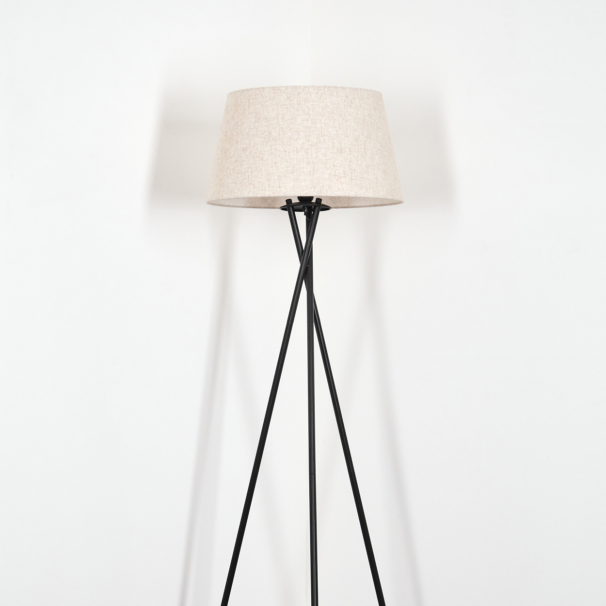 Eine schwarze Metall-Stativ-Stehlampe mit beigem Lampenschirm. Weißer Hintergrund.
