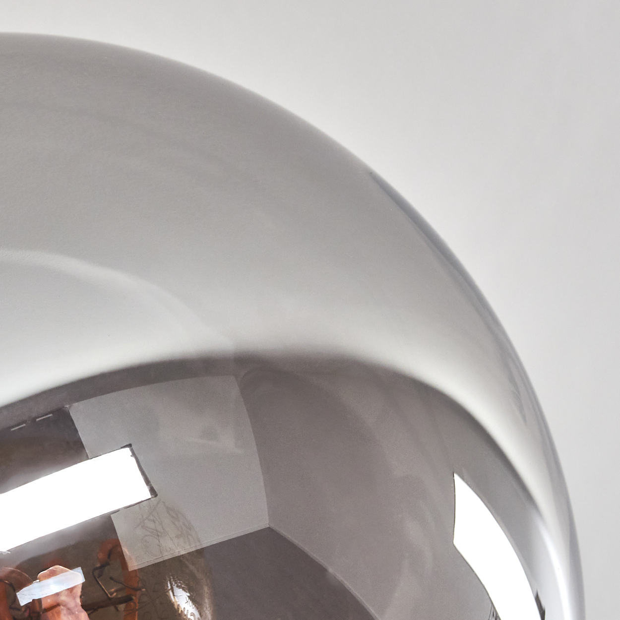Nahaufnahme einer reflektierenden, silbernen Glaskugel. Die Reflexion zeigt ein helles Licht.