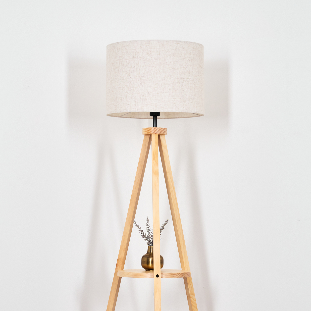 Eine Holz-Stehleuchte mit Beigeschirm vor einer weißen Wand. Eine kleine Vase steht auf dem Regal.