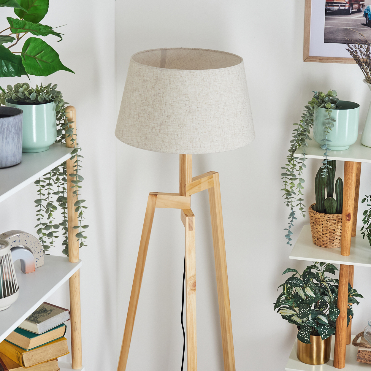 Stehlampe aus Holz mit beigem Schirm. Innenraum mit Regalen, Pflanzen und Dekoration.