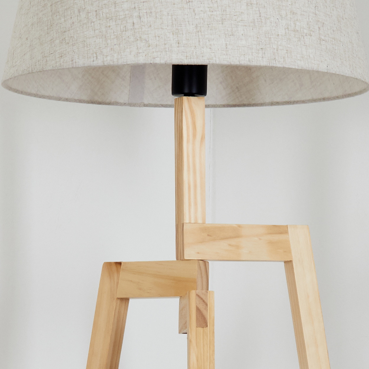 Nahaufnahme einer hölzernen Stativ-Stehlampe. Beiger Schirm und Holzstruktur sind sichtbar. Weißer Hintergrund.