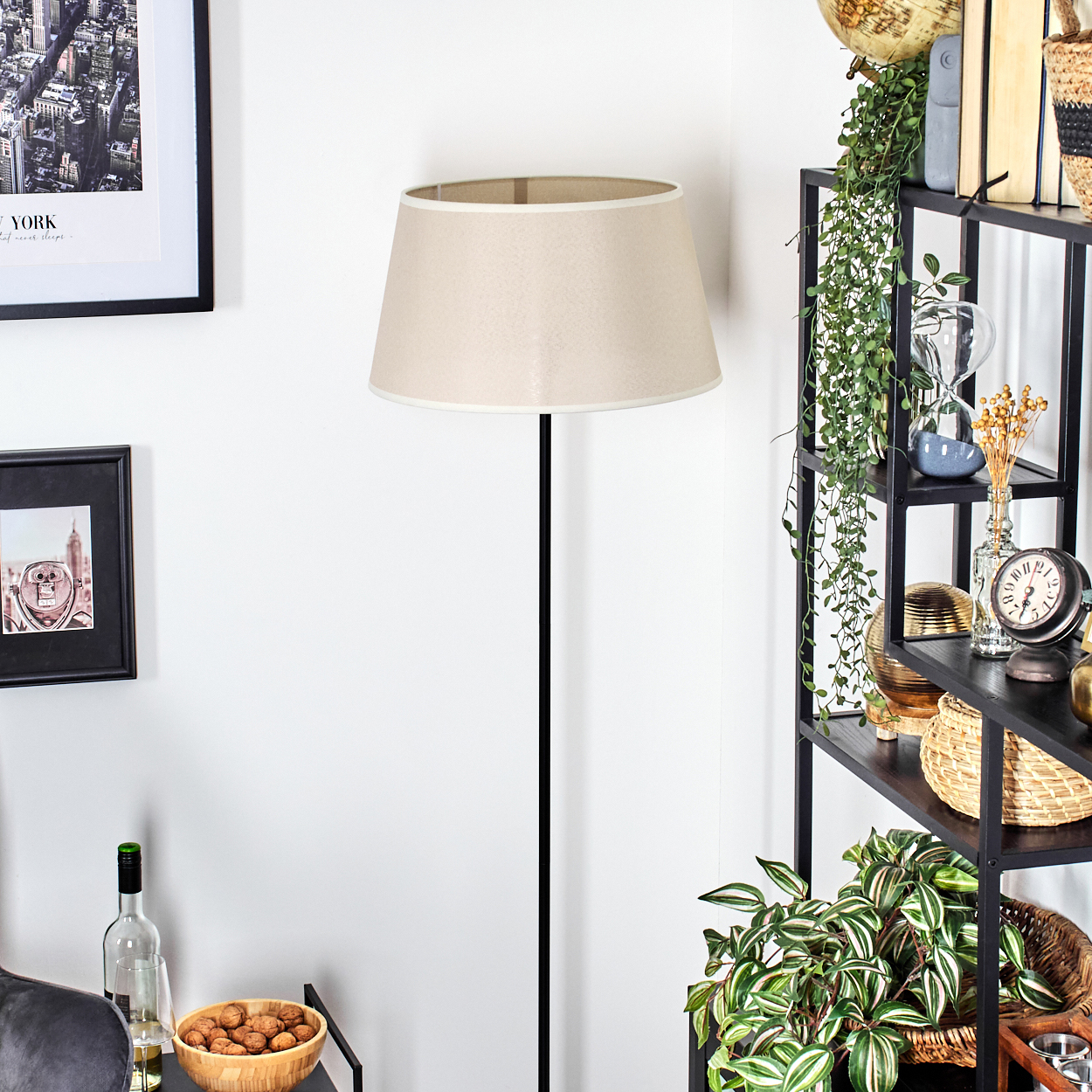 Stehlampe mit schwarzem Mast, beigem Schirm, neben Dekoration und gerahmter Kunst.