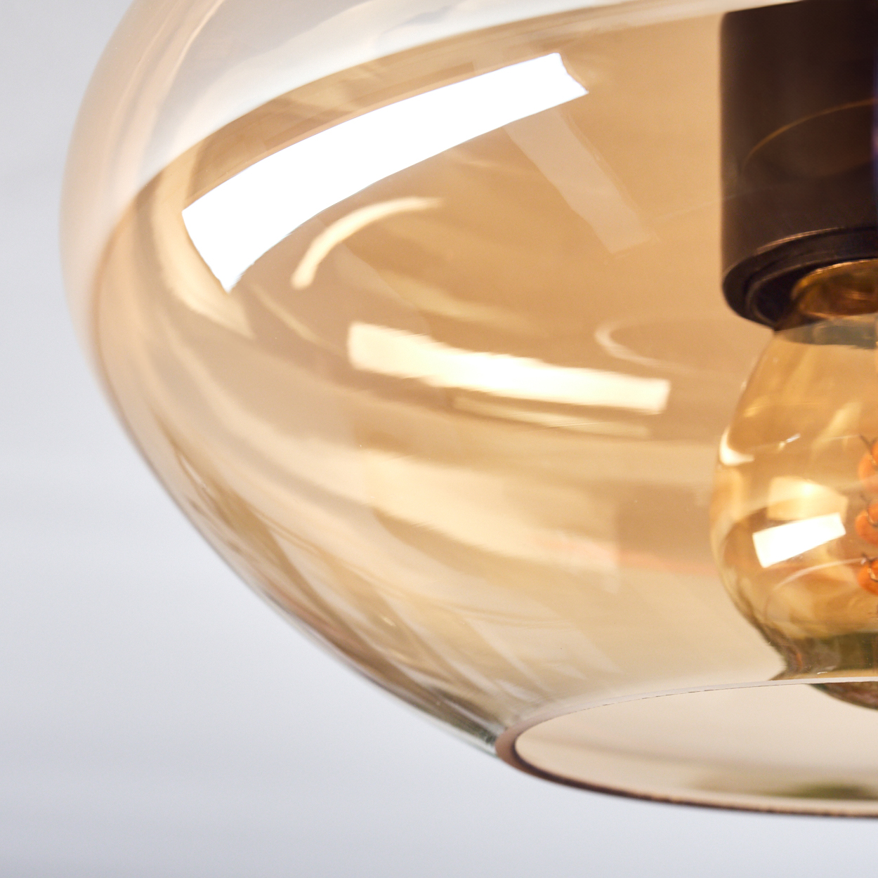 Nahaufnahme des bernsteinfarbenen Glasschirms einer Deckenlampe mit sichtbarer Glühbirne.