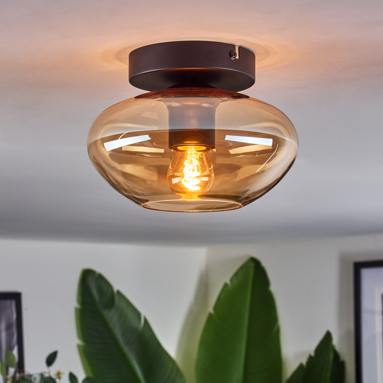 Eine Deckenlampe mit braunem Sockel und bernsteinfarbenem Glasschirm, beleuchtet.